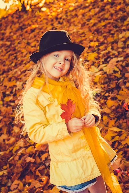 Mała dziewczynka o blond włosach w tle jesień z żółtym liściem