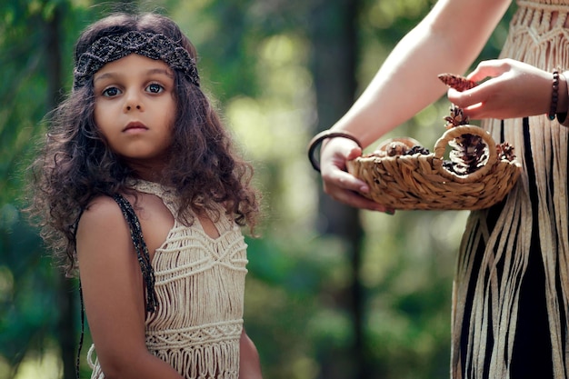 Mała dziewczynka o ciemnych kręconych włosach ubrana jak tubylec w lesie zbiera guzy z matką