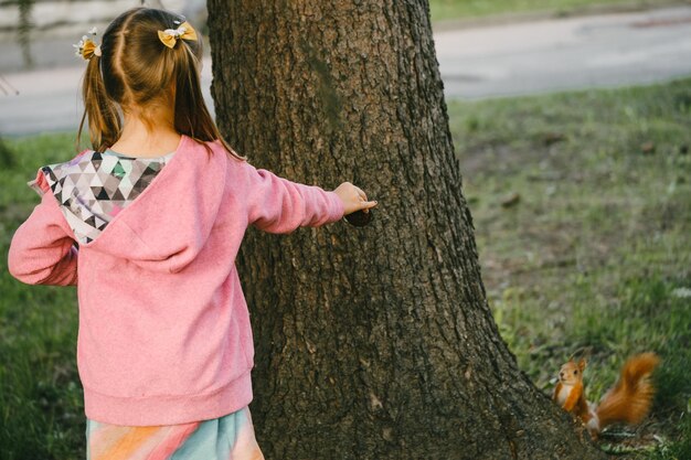Mała dziewczynka patrząca na wiewiórkę w parku.