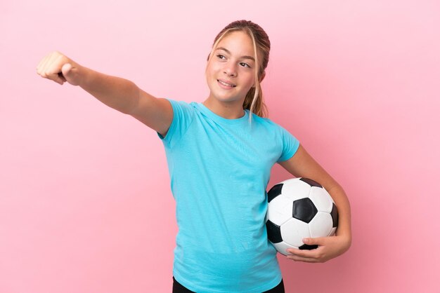 Mała dziewczynka piłkarz odizolowana na różowym tle dająca gest kciuka w górę