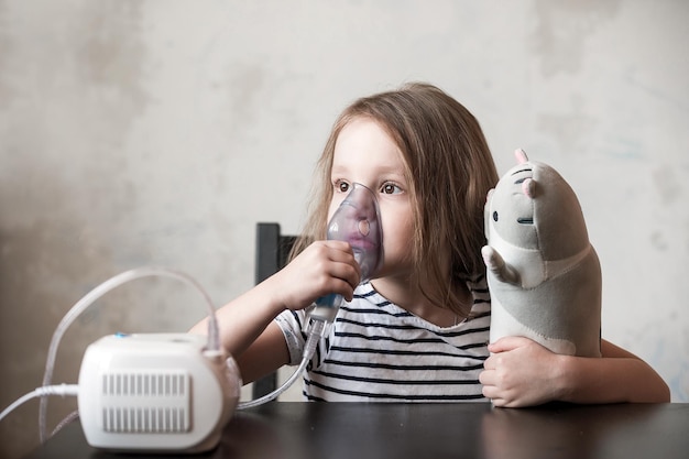 Zdjęcie mała dziewczynka podczas przeziębienia sama siedzi przy stole i robi inhalacje za pomocą urządzenia
