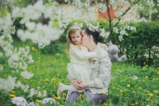 Mała dziewczynka przytula matkę w wiosennym ogrodzie wiśniowym