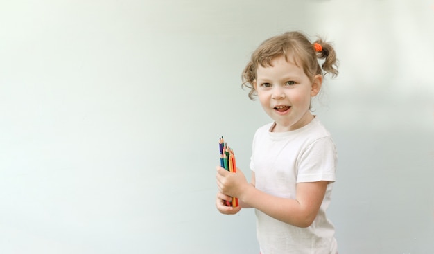 Mała dziewczynka rasy kaukaskiej pięć lat, kręcone blond dziewczynka z kredkami w dłoniach. Pojęcie kreatywności i przygotowania dzieci do szkoły.