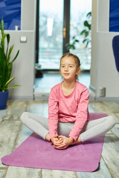 Mała dziewczynka robi ćwiczenia rozciągające ćwiczące jogę na macie fitness w domu