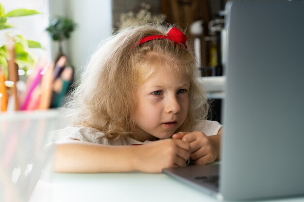 Zdjęcie mała dziewczynka robi lekcje w domu przy laptopie pisze długopisem w zeszycie