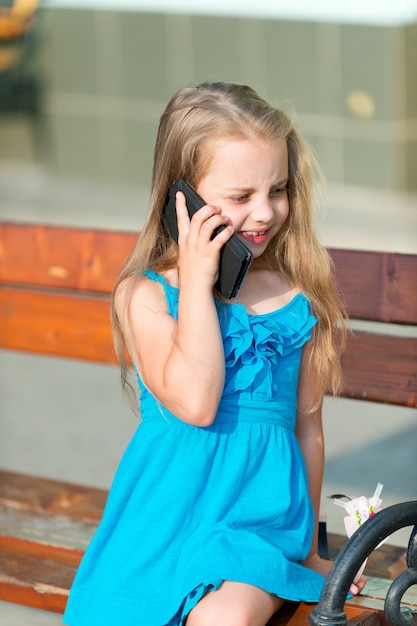 Mała dziewczynka rozmawiać na telefon komórkowy na ławce w parku, lato. Dziecko i nowa technologia, koncepcja dzieciństwa. Komunikacja