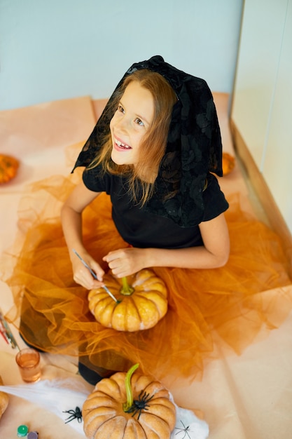 Mała dziewczynka rysująca twarz na pomarańczowej dyni Halloween Jack-O-Lantern
