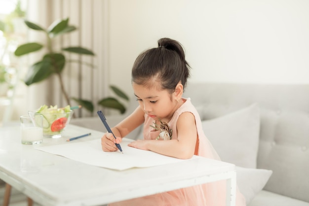 Mała dziewczynka rysuje obraz przy stole z narzędziami do malowania w pomieszczeniu