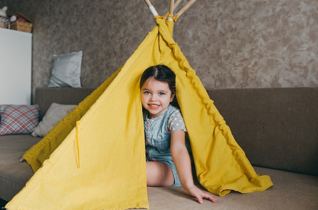 Zdjęcie mała dziewczynka siedzi i uśmiecha się w żółtym tipi. gry domowe i rozrywka dla dzieci
