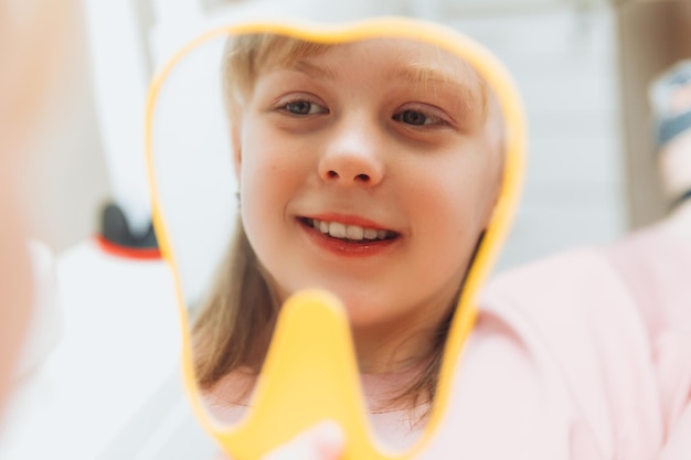 Mała dziewczynka siedzi na fotelu dentystycznym i patrząc w lustro ogląda wyleczone zęby