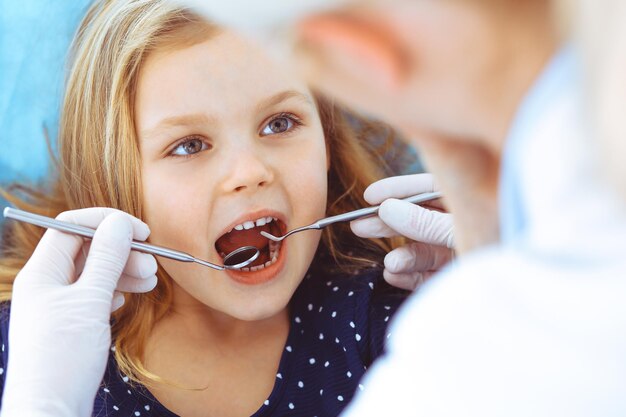 Mała dziewczynka siedzi na fotelu dentystycznym z otwartymi ustami podczas badania jamy ustnej, podczas gdy lekarz. Wizyta w gabinecie stomatologicznym. Koncepcja medycyny. Stonowane zdjęcie.