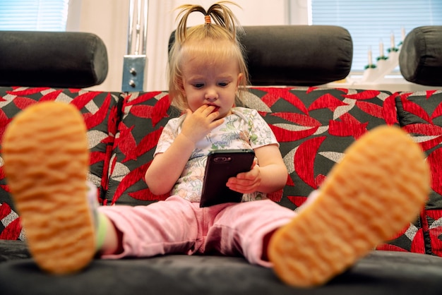 Mała dziewczynka siedzi na kanapie i trzyma smartfona