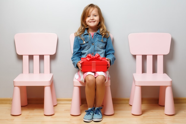 Zdjęcie mała dziewczynka siedzi na krześle i trzyma pudełko z prezentem