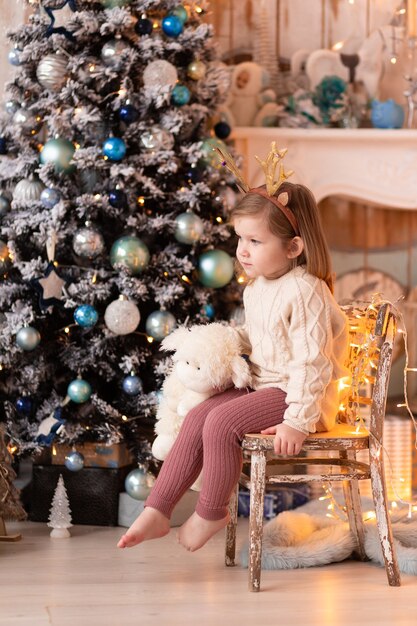 Mała dziewczynka siedzi na krześle na tle nowego roku drzewa