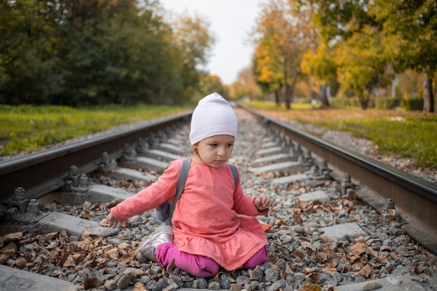 mała dziewczynka siedzi na torach kolejowych. maluch bawi się na kolei w lesie