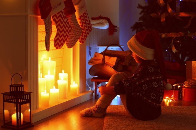 Mała dziewczynka siedzi przy kominku udekorowana na Boże Narodzenie