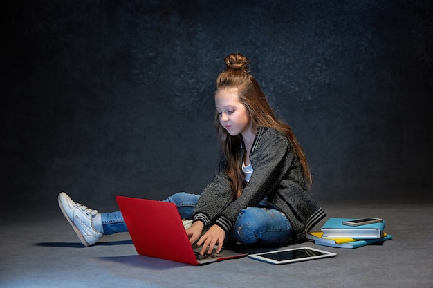 Mała dziewczynka siedzi z laptopem, tabletem i telefonem w szarym studiu