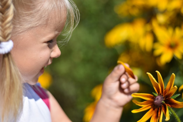Zdjęcie mała dziewczynka śmieje się i zrywa płatek z żółtego kwiatu stokrotki