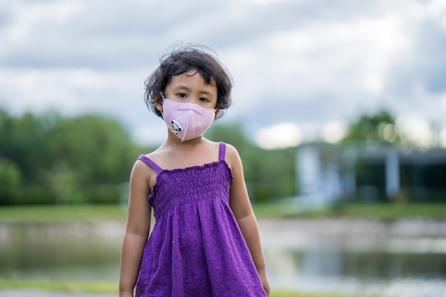 Mała dziewczynka smutny wyraz twarzy nosząca maskę ochronną chodzącą po polu