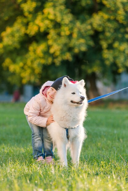 Mała dziewczynka spaceruje ze swoim psem Samoyedem po parku jesienią