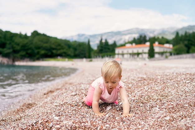 Mała dziewczynka stoi na kolanach na kamienistej plaży w pobliżu willi na wodzie milocer