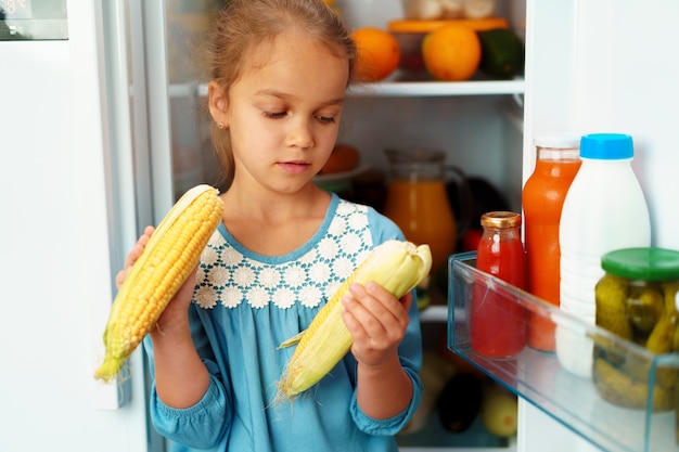 Mała dziewczynka stoi przed lodówką i wybiera jedzenie