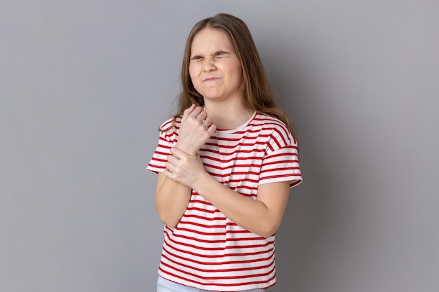 Mała dziewczynka stojąca z grymasem bólu masująca obolały nadgarstek cierpiący na uraz dłoni lub zwichnięcie