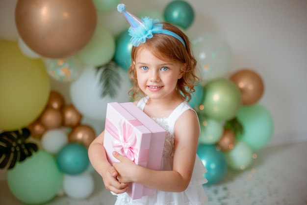 Mała dziewczynka świętuje urodziny na tle balonów trzymających prezent