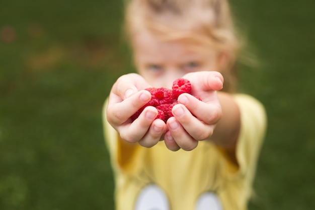 Mała dziewczynka trzyma garść czerwonych jagódmalin