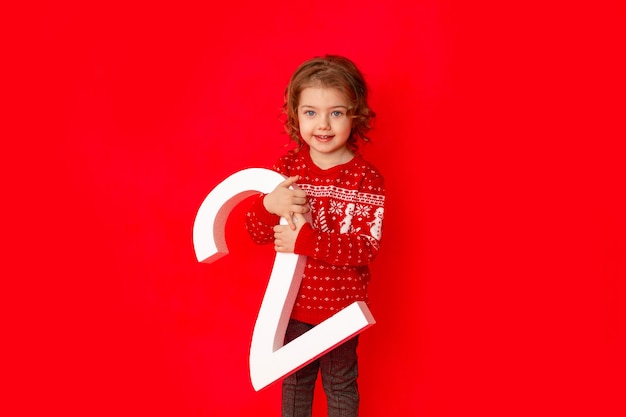 Mała Dziewczynka Trzyma Numer Dwa W Zimowe Ubrania Na Czerwonym Tle, Miejsca Na Tekst