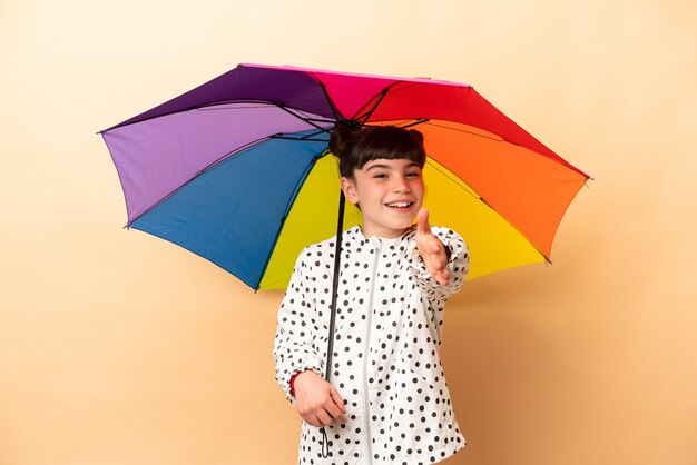 Mała dziewczynka trzyma parasol na białym tle na beżowej ścianie, ściskając ręce za zamknięcie dużo