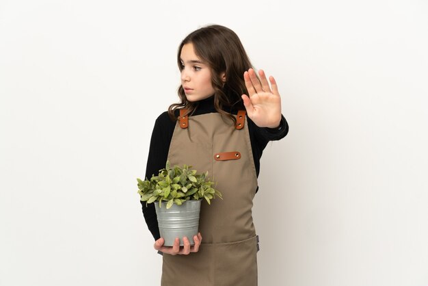 Mała dziewczynka trzyma roślinę na białym tle, robiąc gest zatrzymania i rozczarowana