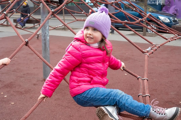 Mała dziewczynka trzyma się lin na placu zabaw w parku