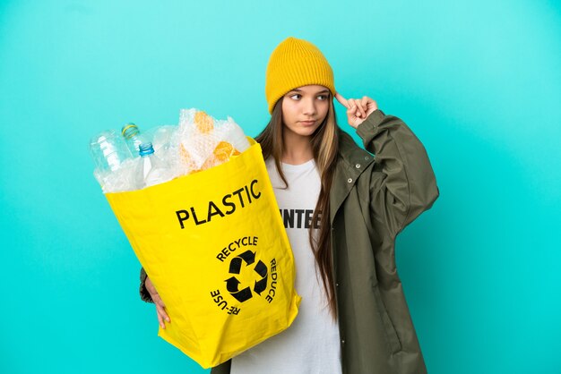 Mała dziewczynka trzyma torbę pełną plastikowych butelek do recyklingu na odizolowanym niebieskim tle, ma wątpliwości i myśli