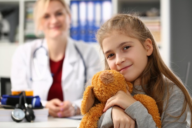 Mała dziewczynka trzyma zabawkę niedźwiedzia na wizytę lekarską z pediatrą