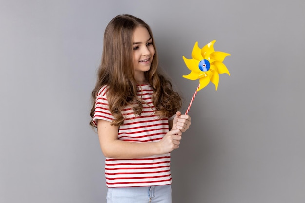 Mała dziewczynka uśmiecha się beztrosko do kamery trzymając papierowy wiatrak wiatraczek zabawka na patyku