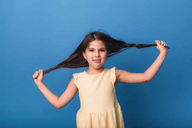 Mała dziewczynka uśmiecha się i ciągnie za długie splecione włosy na niebieskim tle