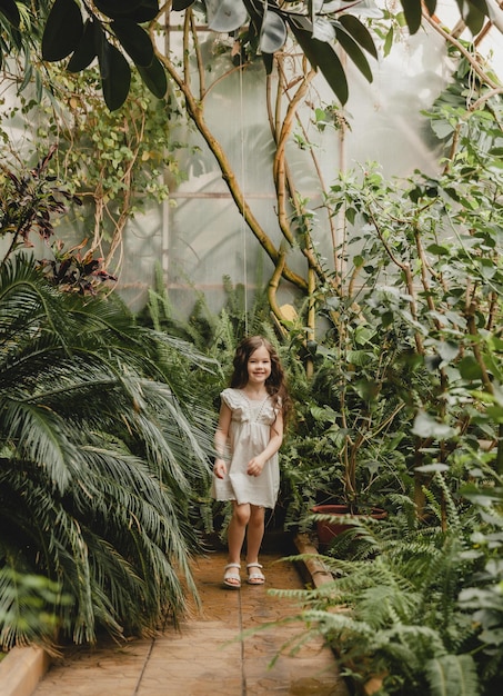 Mała dziewczynka w białej sukience biegnie ścieżką w ogrodzie botanicznym