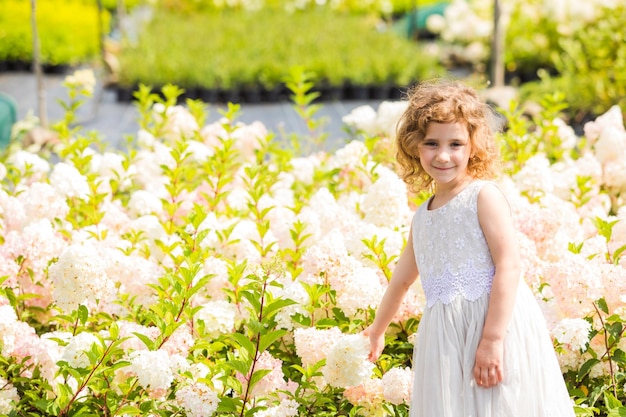 Mała dziewczynka w białej sukience w pobliżu różowych kwiatów hortensji Dziecko zbiera świeże kwiaty dla matki na targu roślin na świeżym powietrzu