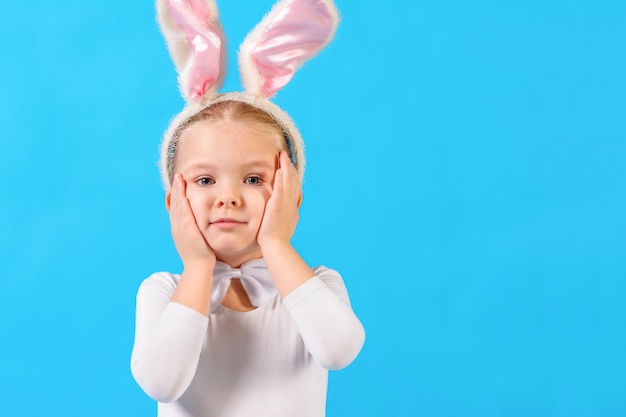 Mała dziewczynka w białym królika kostiumu na błękitnej ścianie. Dziecko trzyma głowę.