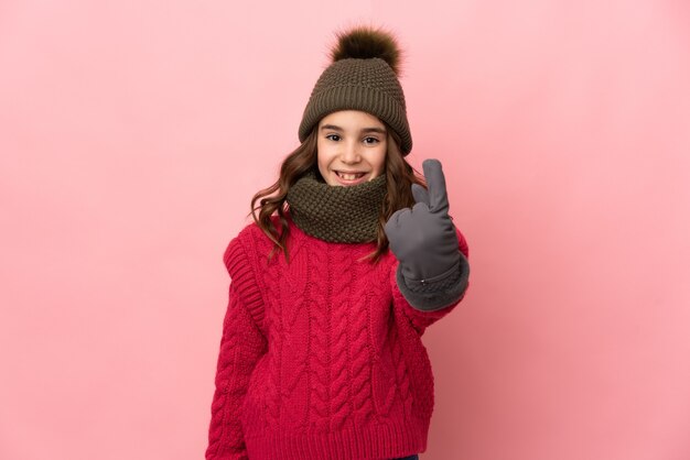 Mała dziewczynka w czapkę zimową na białym tle na różowym tle robi nadchodzący gest