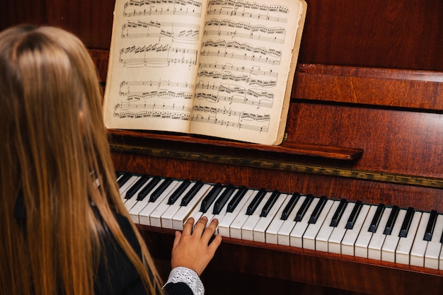 Mała Dziewczynka W Czarnej Sukience Uczy Się Grać Na Pianinie. Dziecko Gra Na Instrumencie Muzycznym.