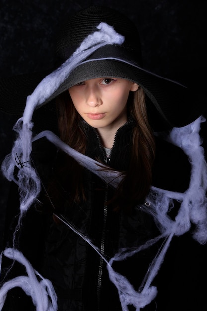 Zdjęcie mała dziewczynka w czarnym kapeluszu na halloweenowej pajęczynie