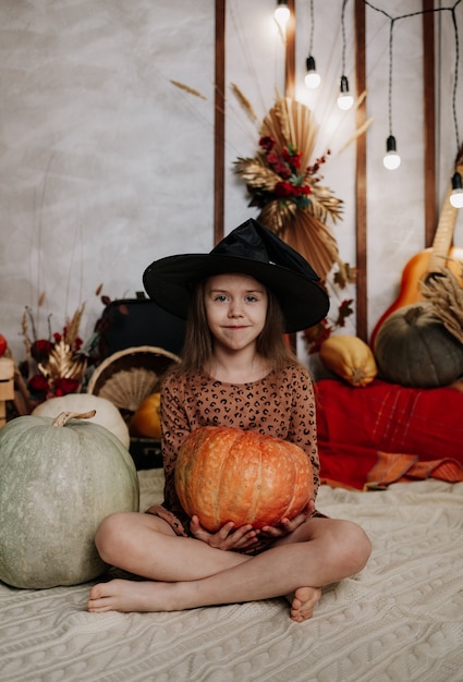 Mała dziewczynka w czarnym kapeluszu siedzi na dzianinowym kocu w dynie