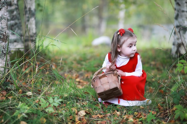 Mała dziewczynka w czerwonej czapce i sukienkach spaceruje po parku Cosplay dla bajkowego bohatera Czerwonego Kapturka