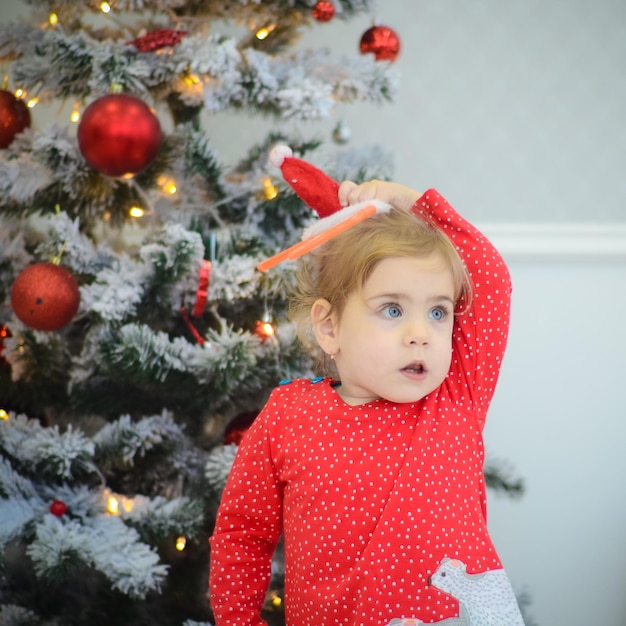 Zdjęcie mała dziewczynka w czerwonej sukience bawiąca się w pokoju z dekoracjami świątecznymi