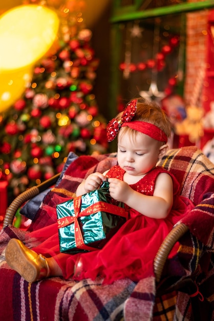 Mała dziewczynka w czerwonej sukience otwiera prezent noworoczny
