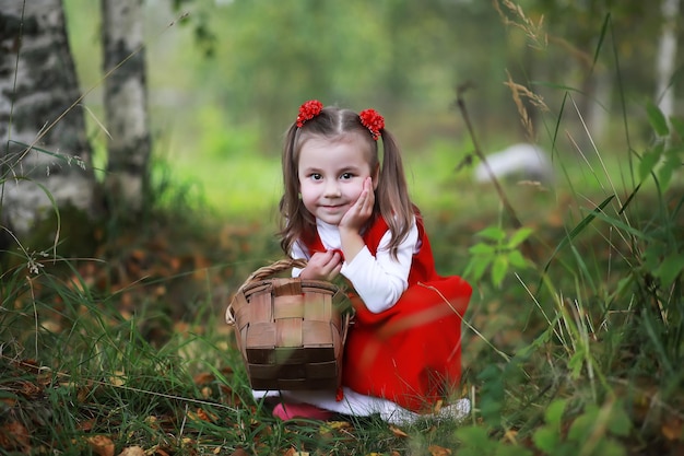 Mała dziewczynka w czerwonym kapeluszu i sukienkach spaceruje po parku. Cosplay dla bajkowego bohatera „Czerwony Kapturek”