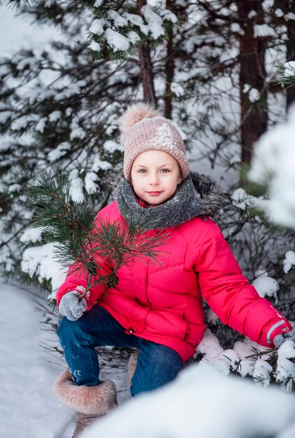 Mała dziewczynka w jasnej kurtce bawi się w zimowym śnieżnym lesie.