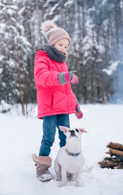 Mała Dziewczynka W Jasnej Kurtce Bawi Się W Zimowym, Zaśnieżonym Lesie Ze Swoim Psem Jack Russell Terrierem